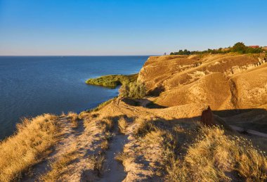 Muhtemelen Ukrayna 'nın Kherson bölgesindeki kıyı kayalıkları ve deniz manzarası. Kuru, çimenli tepeler mavi sularla buluşur. Açık mavi gökyüzü. Önceki bağlama göre