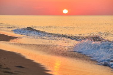 Güneş sakin bir okyanusun üzerinde yükseliyor, yumuşak dalgalar kumlu bir plaja vuruyor..
