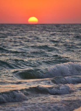 Okyanus dalgaları canlı bir altın gün batımında kıyıya çarpıyor. Doğal fotoğraf, sıcak tonlar, arka plan için uygun..