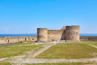 Önplanda kır çiçeklerinin büyüdüğü taş bir kule ve Akkerman Kalesi (Bilhorod-Dnistrovskyi Kalesi) içindeki duvarların görüntüsü.