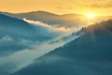 Dağ katmanlarının üzerinde sersemletici bir gün doğumu, parlak güneş ışınları vadilerdeki kalın sisleri delip geçiyor. Atmosferik vahşi manzara silueti. Umut dolu sahne.