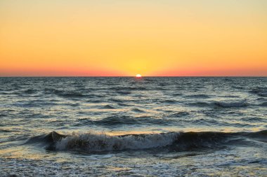 Canlı bir günbatımı gökyüzünün altında okyanus dalgaları. Güneş ufukta batıyor. Deniz manzarası, doğa manzarası..