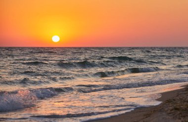 Okyanus dalgaları canlı bir altın gün batımında kıyıya çarpıyor. Doğal fotoğraf, sıcak tonlar, arka plan için uygun..