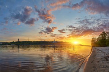 Gün batımında Ukrayna, Kyiv 'in panoramik manzarası. Dnipro Nehri renkli gökyüzünü yansıtır, şehir manzarası ve Anavatan Anıtı uzaklardan görülebilir.