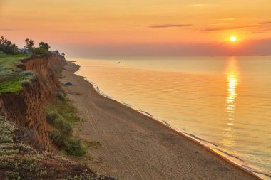 Kıyı kayalıklarının yakınındaki kumlu bir plajda kamp çadırları kurulmuş. Deniz üzerinde canlı bir gündoğumu varmış..