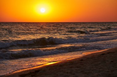 Okyanus dalgaları canlı bir altın gün batımında kıyıya çarpıyor. Doğal fotoğraf, sıcak tonlar, arka plan için uygun..
