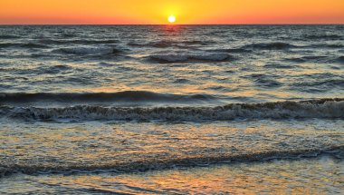 Canlı bir günbatımı gökyüzünün altında okyanus dalgaları. Güneş ufukta batıyor. Deniz manzarası, doğa manzarası..