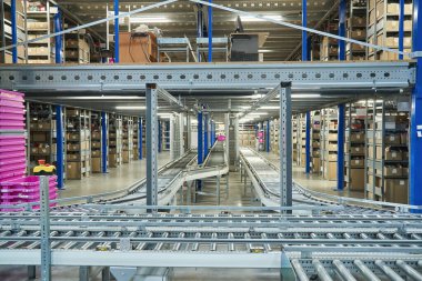 Interior view of a large, automated warehouse with multi-level shelving packed with inventory and intricate conveyor belt systems running through the aisles. Modern logistics.