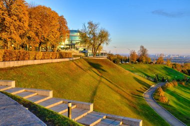 Günbatımının sıcak, altın ışığı Ukrayna 'nın başkenti Kyiv' deki Sonsuzluk Parkı 'nın (Slava Park) dik, manikürlü çimenli yamaçlarında sonbahar boyunca uzun gölgeler bırakır..
