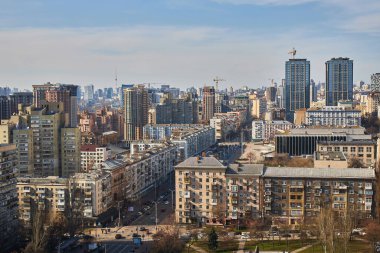A bustling tree-lined boulevard in modern Kyiv on a sunny day, with cars in traffic, pedestrians on sidewalks, and contemporary buildings in the background.