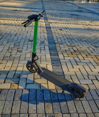 electric scooters with green steering columns are parked on a cobblestone square in a city during the golden hour. A modern, eco-friendly urban transportation solution.
