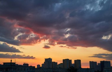Alacakaranlıkta şehir siluetinin silueti, binaların karanlık şekillerini içeren turuncu, pembe ve koyu mavi gökyüzü dağınık bulutlar ve şehir ışıkları.