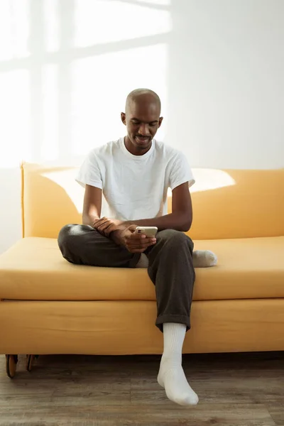Junger Schwarzer Mann Entspannt Sich Hause Mit Seinem Handy Auf lizenzfreie Stockbilder