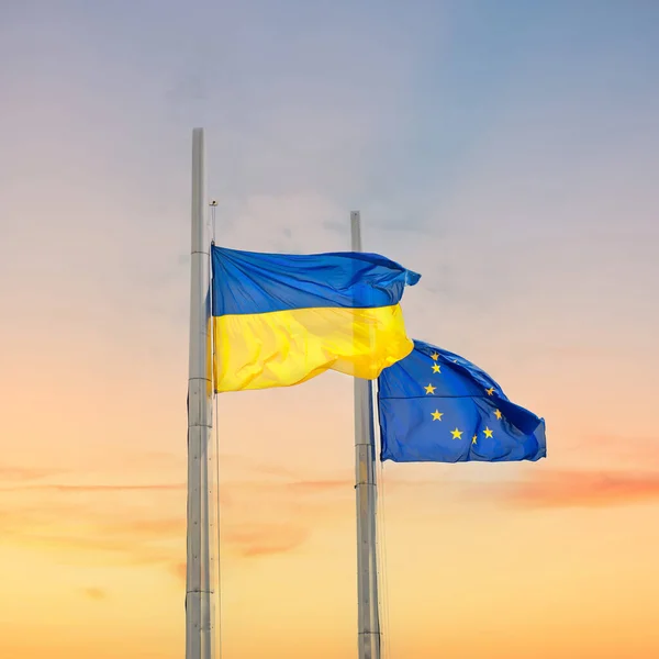 stock image Flags of Ukraine and Europe on poles with sunset sky