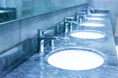 Umumi tuvaletin içi beyaz seramik lavabo, ayna ve musluklarla dolu.