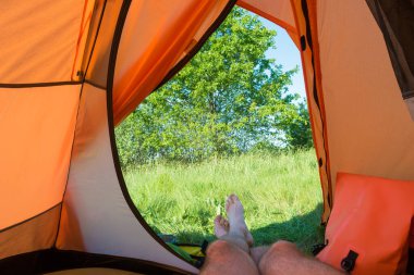 Turuncu çadırda yeşil çimenli yeşil çimlere uzanan bir adam.