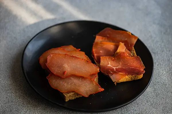 Toasts with rye bread and meat slices on the plate on concrete table