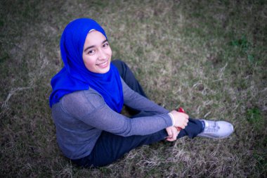 Gülümseyen genç bir bayan çimenlerde tek başına oturuyor.