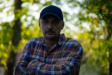 Taşrada kollarını kavuşturan kareli tişörtlü, kendinden emin olgun bir adam. Yüksek kalite fotoğraf