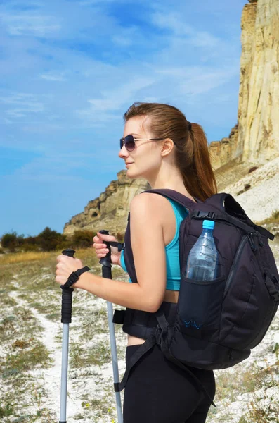 Happy young woman with backpack and trekking poles in mountains.