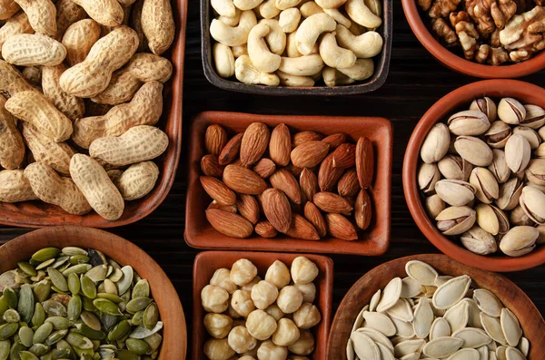 Flat lay view at assorted nuts and seeds in clay bowls on wooden kitchen table