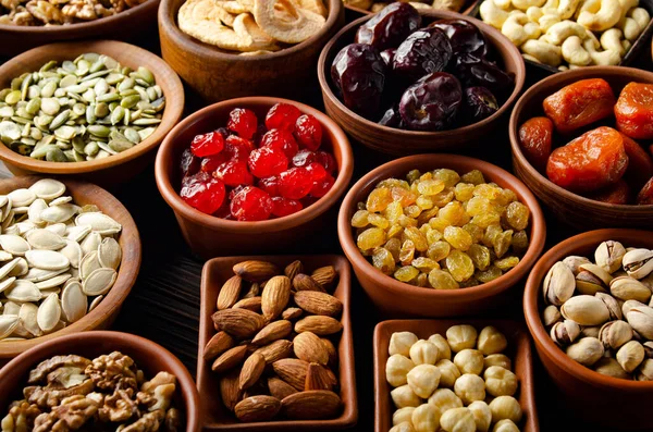 Assorted nuts seeds and dehydrated fruits in bowls on wooden kitchen table