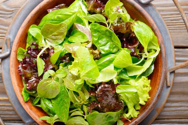 Top view at clay dish with green and violet lettuce, lamb\'s lettuce salad with oregano flowers on vintage metal tray