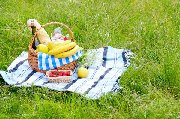 Picnic basket with fruits wine and bread on the grass with strawberry aside