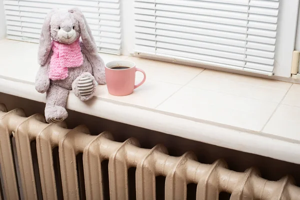 咖啡杯和柔软的玩具坐在霍尔热水器散热器的窗台上 图库图片