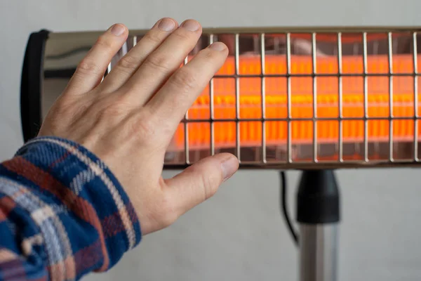 Caucasian male warming up hand near infrared heater. Space for text