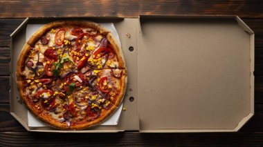 Pepperoni pizza with bell peppers sweetcorn and arugula in open carton box on dark wooden table flat lay with copy-space clipart