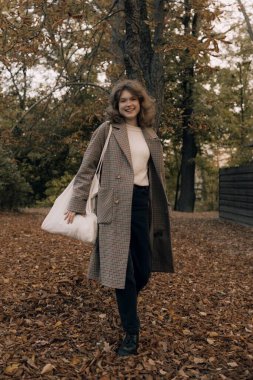 Sonbaharda parkta neşeli bir kızın portresi. Dışarıda palto giyen mutlu kız. Ilık sonbahar ve açık havada yürüyüş kavramı.