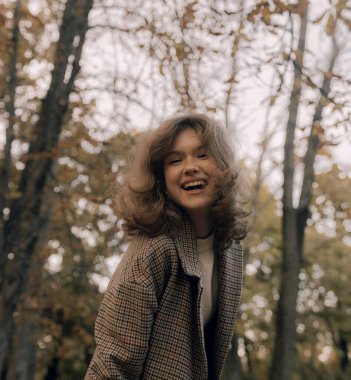 Sonbaharda parkta neşeli bir kızın portresi. Dışarıda palto giyen mutlu kız. Ilık sonbahar ve açık havada yürüyüş kavramı.