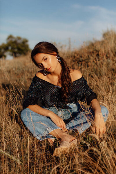 Fashionable young model in boho style clothes on a background of dry grass, field. Female beauty and style concept. Advertisement or clothes sale design.
