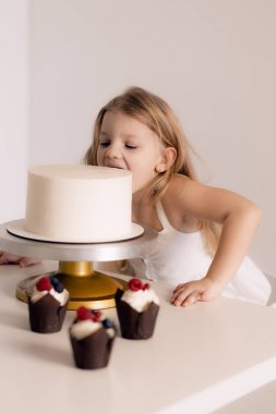 Beautiful happy little girl biting birthday cake. Looking at cakes. Festive and holiday concept.