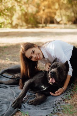 Beautiful happy young woman sitting on the grass hugging a dog. Love and affection for pets, friendship companion. dog breed - cane corso