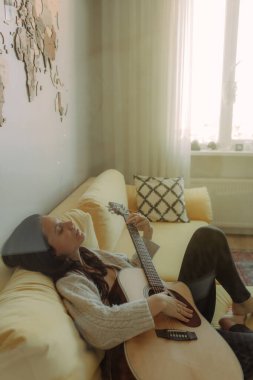 Yaratıcı hobi. Yetenekli genç bayan müzisyen koltuğunda tek başına oturup klasik gitar kullanarak enstrümantal bir şarkı besteler. Gülümseyen bayan müzik aletinde sakin bir melodi çalar. Boşluğu kopyala