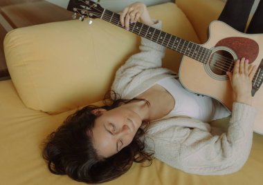 Yaratıcı hobi. Yetenekli genç bayan müzisyen koltuğunda tek başına oturup klasik gitar kullanarak enstrümantal bir şarkı besteler. Gülümseyen bayan müzik aletinde sakin bir melodi çalar. Boşluğu kopyala