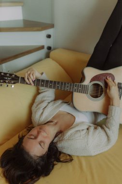 Yaratıcı hobi. Yetenekli genç bayan müzisyen koltuğunda tek başına oturup klasik gitar kullanarak enstrümantal bir şarkı besteler. Gülümseyen bayan müzik aletinde sakin bir melodi çalar. Boşluğu kopyala