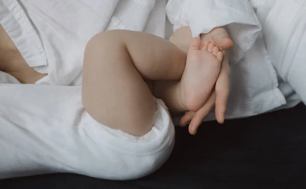 妈妈的手牵着新生婴儿的腿抚摸着 快乐孕产和新生儿护理的概念 — 图库照片