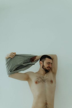 Mutlu gülümseyen genç adam beyaz tişörtünü çıkarıyor. Kas geri geldi..