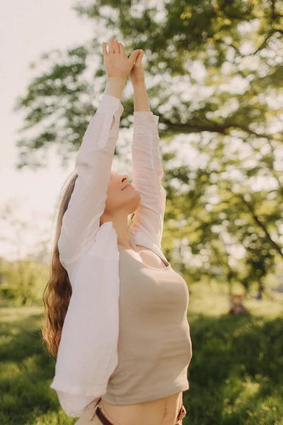 Parkta güneş ışığıyla yoga. Genç kadın gökyüzüne uzanıyor. Sakinlik ve meditasyon kavramı. Sağlıklı yaşam tarzı kavramı.