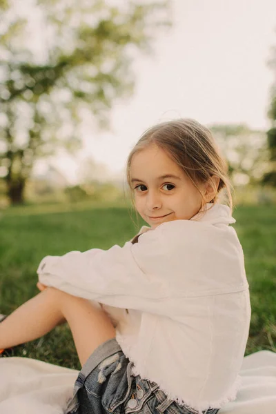 緑の森の中で新鮮な空気を呼吸する小さなリラックスした女の子 夏の晴れた日に公園の外の緑の草の上に座って白い服の少女の間にかなり 魅力的なウクライナの子供の肖像画 — ストック写真