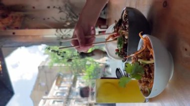 Sokak yemeği. Tabakta büyük bir porsiyon Tayland eriştesi. Yakın plan bir kadın, Tayland 'daki bir kafedeki tabaktan Asya eriştesi almak için çubuk kullanıyor..