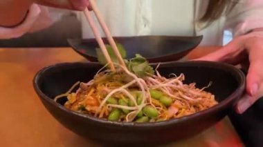 Sokak yemeği. Tabakta büyük bir porsiyon Tayland eriştesi. Yakın plan bir kadın, Tayland 'daki bir kafedeki tabaktan Asya eriştesi almak için çubuk kullanıyor..