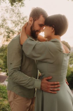 Hamile çift doğada sarılıyor. Parkta yürüyen hamile karısı olan bir koca. Mutlu aile konsepti fotoğrafı. Odak bulanıklığı ve gürültü efekti yok
