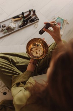 Kadın yoga minderinde otururken Tibet şarkı kasesinde oynuyor. Antika tonlu. Yumuşak odak bulanık ve gürültü efekti.