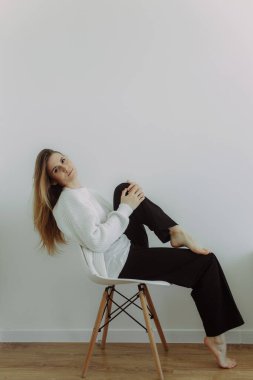 A young girl immersed in her thoughts sits on a chair on a white background, space for text. The concept of self-knowledge. Visual content for psychotherapists and coaches