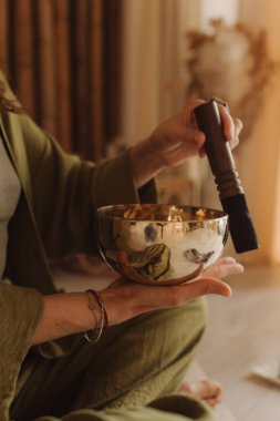 Kadın yoga minderinde otururken Tibet şarkı kasesinde oynuyor. Antika tonlu. Yumuşak odak bulanık ve gürültü efekti.