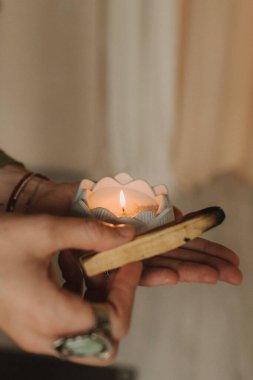 Genç bir kadın elinde sigara içen bir Palo Santo sopası tutuyor. Budist şifa uygulamaları. Boşluğu negatif enerjiden temizliyorum. Aromaterapi. Seçici odaklanma, kapat. Yumuşak odak ve gürültü etkisi.